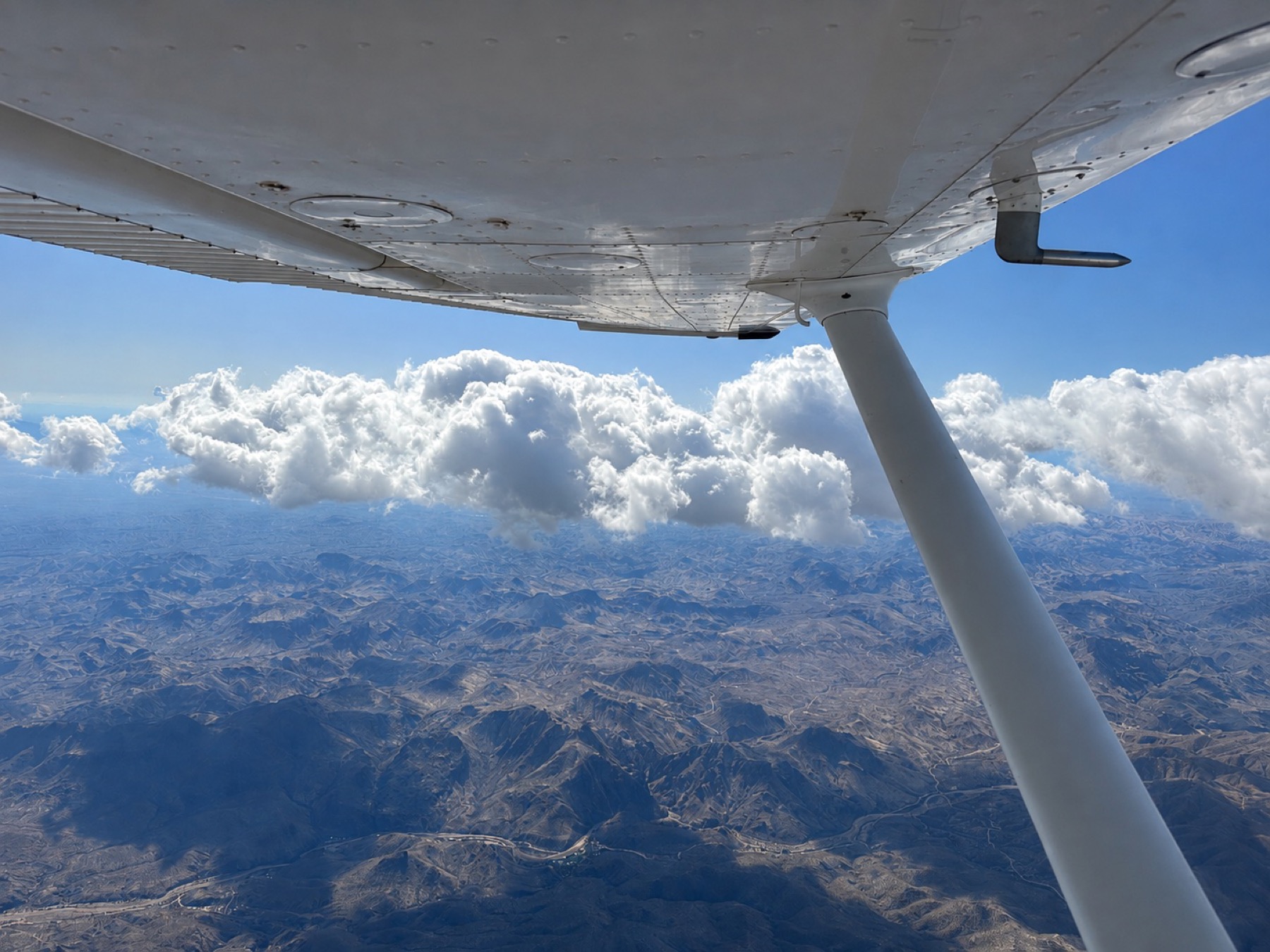 Wing view over clouds and mountain terrain