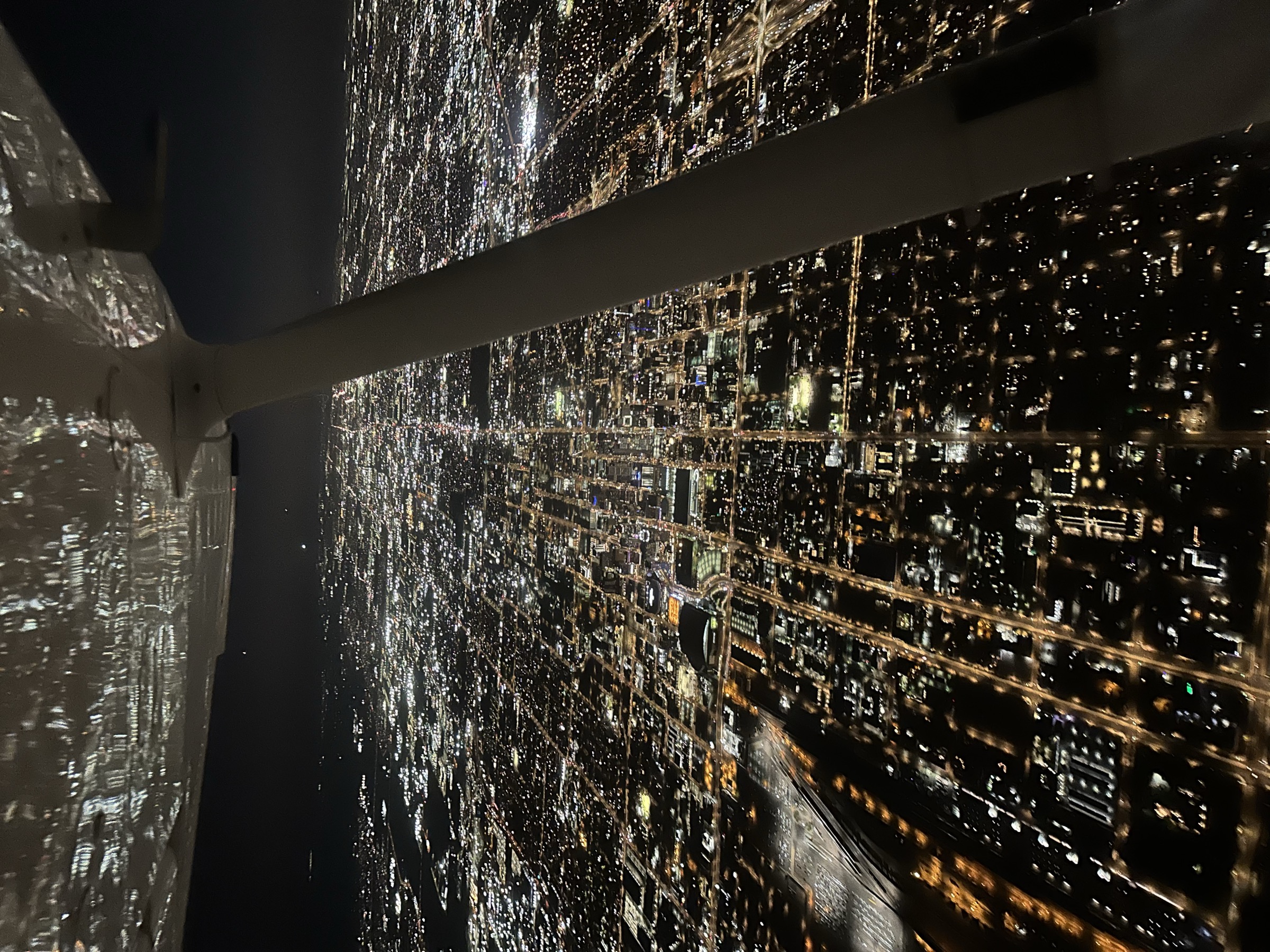 Aircraft wing silhouetted against city lights at night